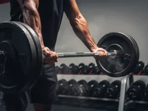 Atleet tilt een zwaar beladen barbell in een moderne gym, krijtpoeder zweeft in de lucht, dramatische belichting op gespierde onderarmen.