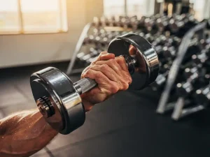 Gespierde onderarm die een zware dumbbell curl uitvoert in een moderne sportschool met gouden zijlicht.