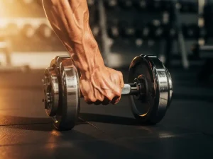 Gespierde arm met zichtbare aderen die een stalen dumbbell curl uitvoert in een moderne gym, warm gouden licht.