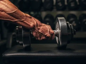 Gespierde onderarm met zichtbare aderen houdt een zware dumbbell vast op een gymbank, dramatisch zijlicht benadrukt spierspanning.