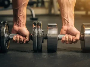 Gespierde onderarm die een zware halter vastgrijpt naast een arm met lichte dumbbell, close-up bicepscurl in gym.
