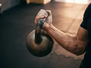 Gespierde onderarm met krijtpoeder houdt een gietijzeren kettlebell vast tijdens een curl in een moderne sportschool.